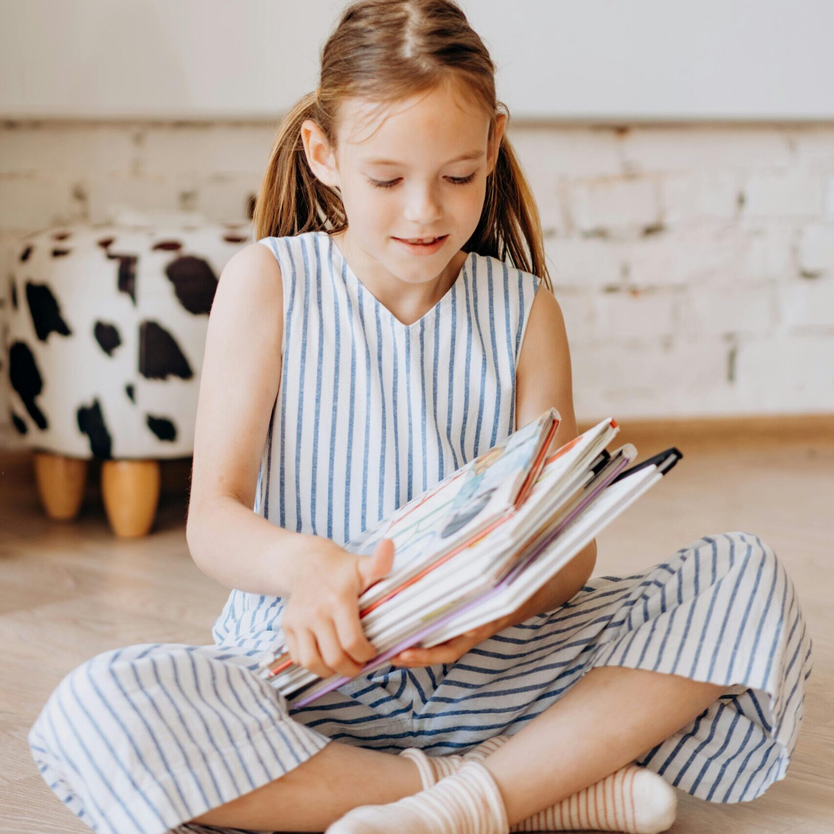A young girl in striped clothing reads a book indoors, showcasing childhood learning.